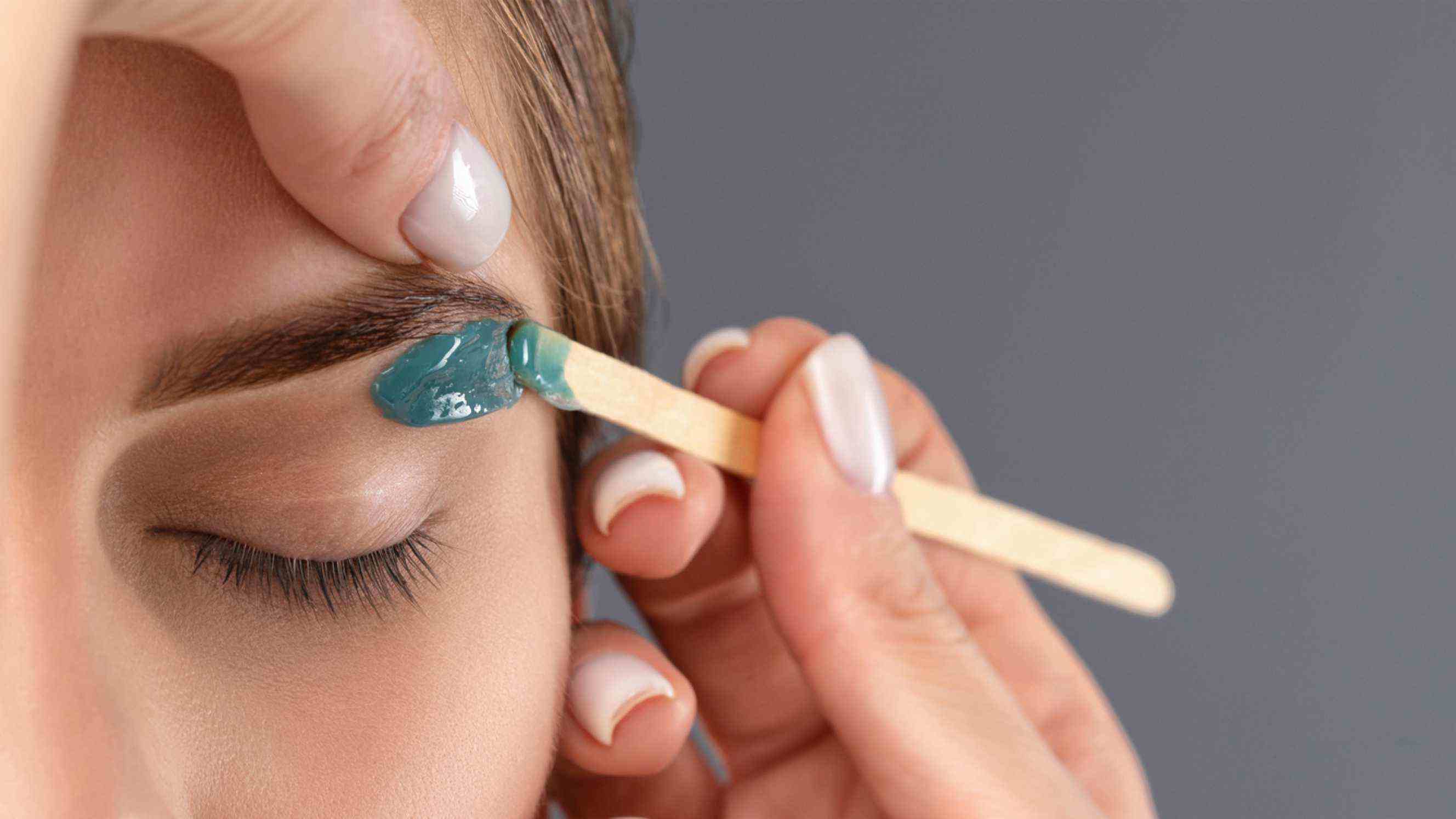 A beautician carefully applying wax to shape a client's eyebrows, representing precise eyebrow waxing services near you.