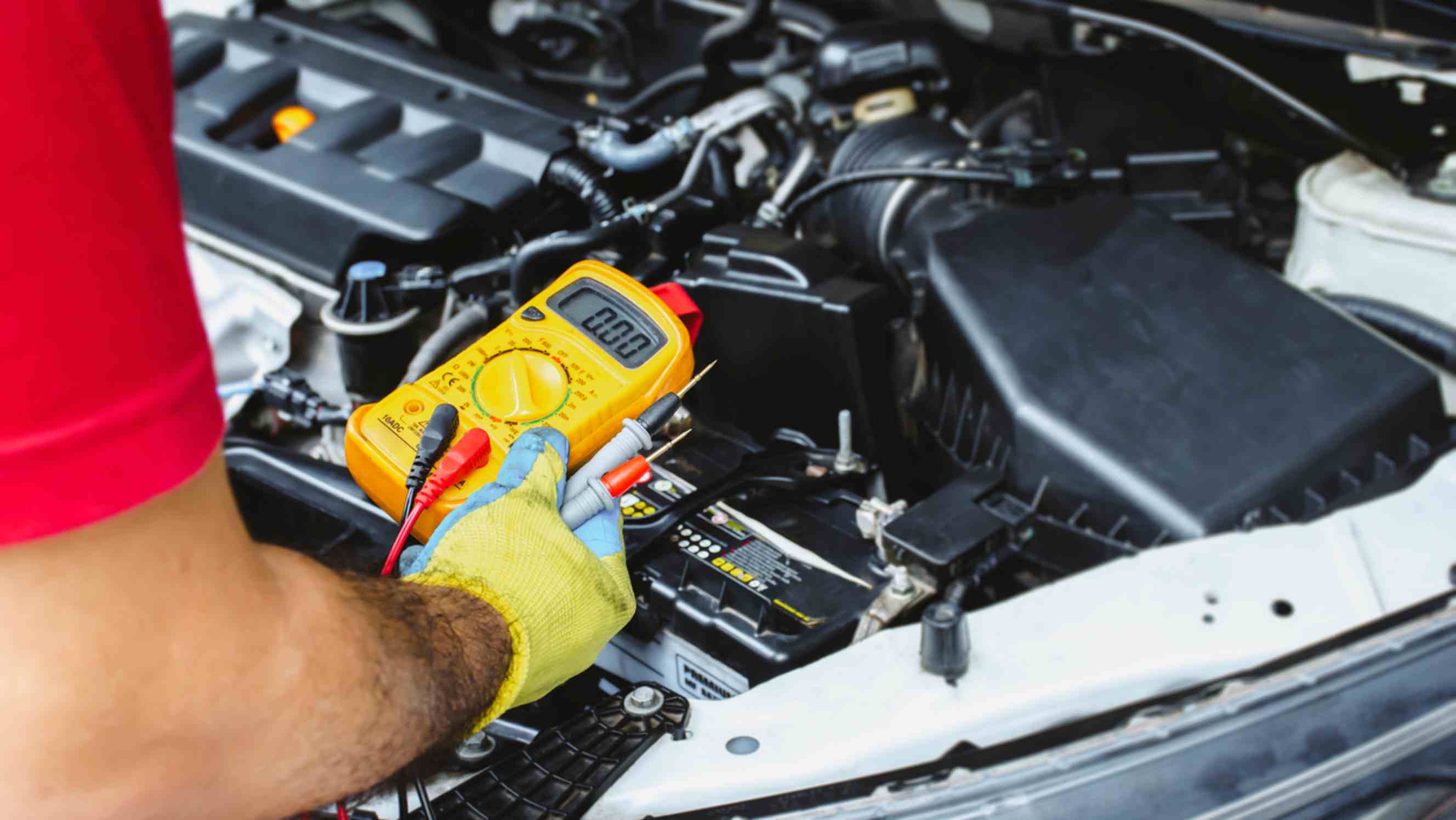 A technician performing car electrical repair near you, using a multimeter to check the voltage of the car’s battery