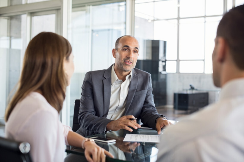 advisory-vs-consulting – professional man addressing two clients in a modern meeting room