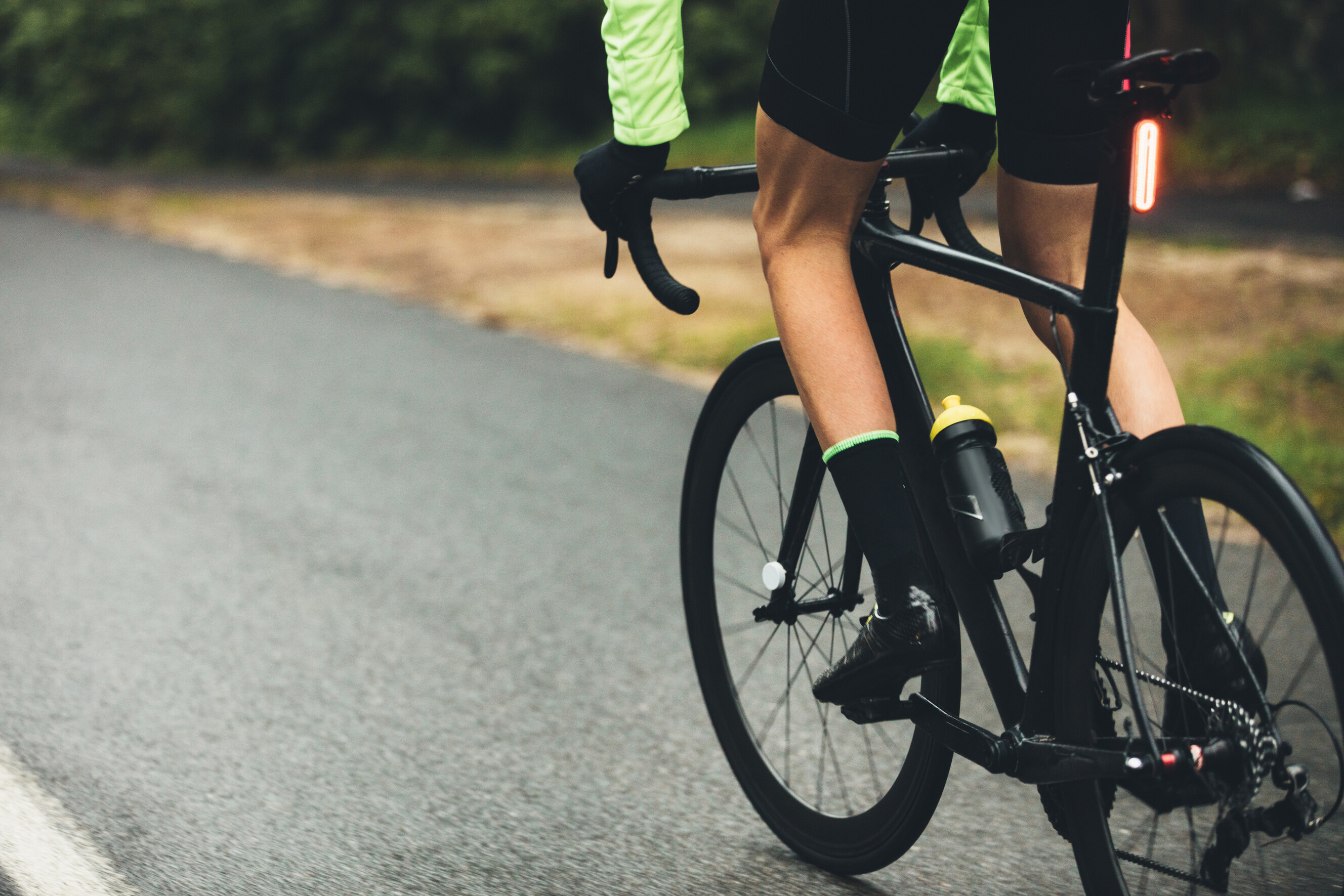 Cyclist riding a black road bike on a wet asphalt road.