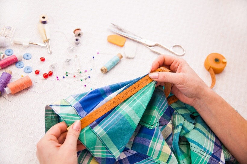 Alterations cost - Person measuring a plaid shirt for clothing alterations with sewing tools nearby.