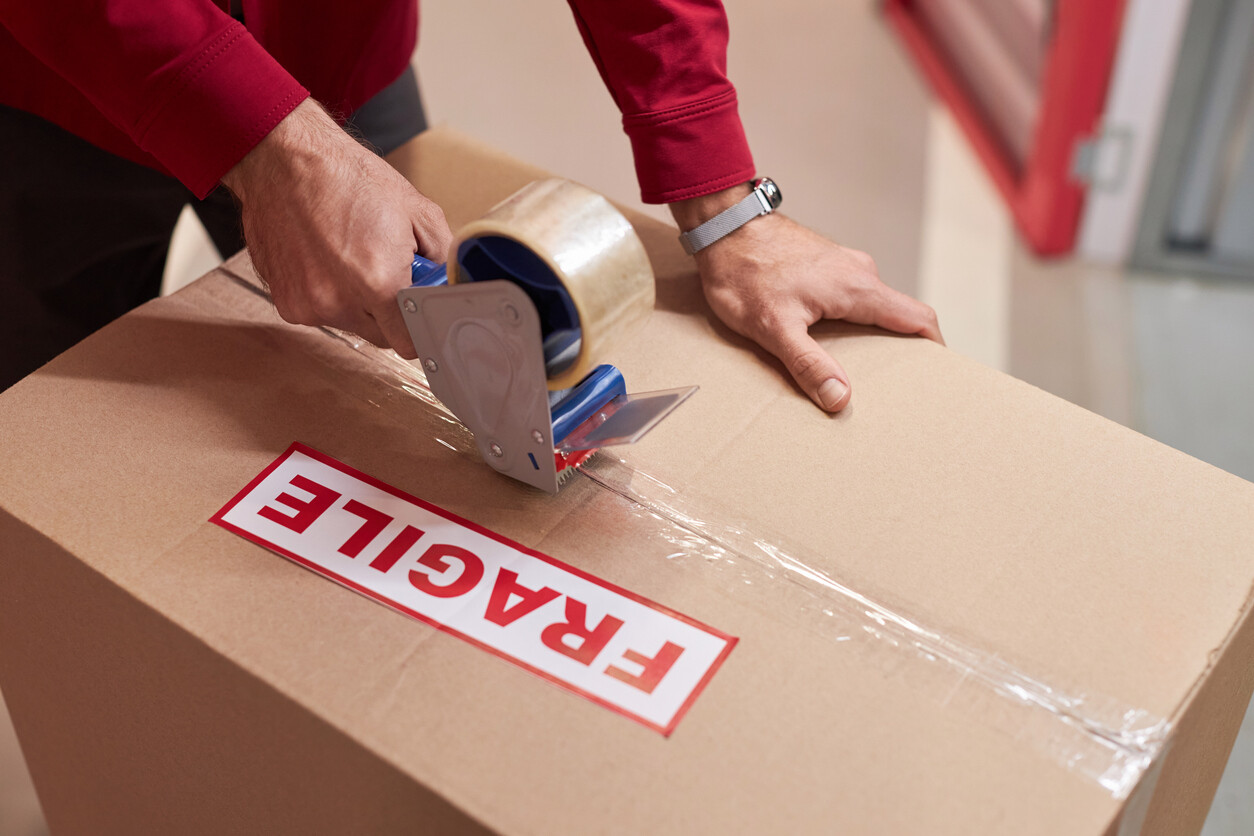 Fragile removals expert sealing a cardboard box with tape, preparing delicate items for safe transport during a professional removals service