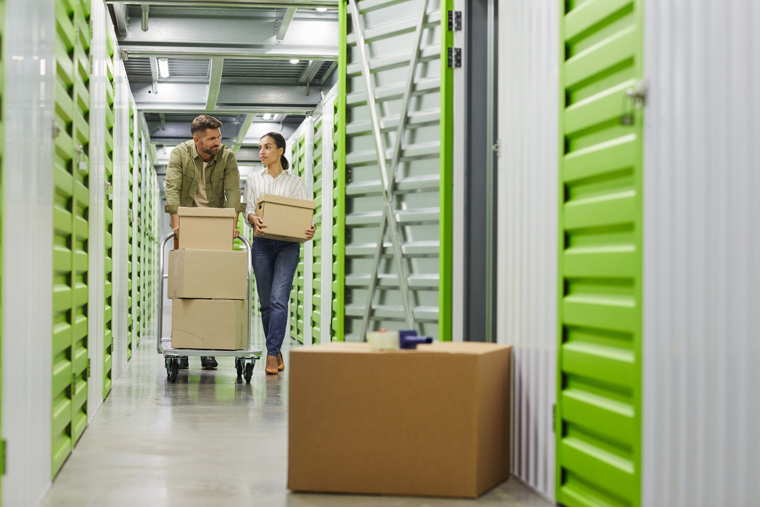 Movers transporting packed boxes into a climate-controlled storage unit using a dolly.