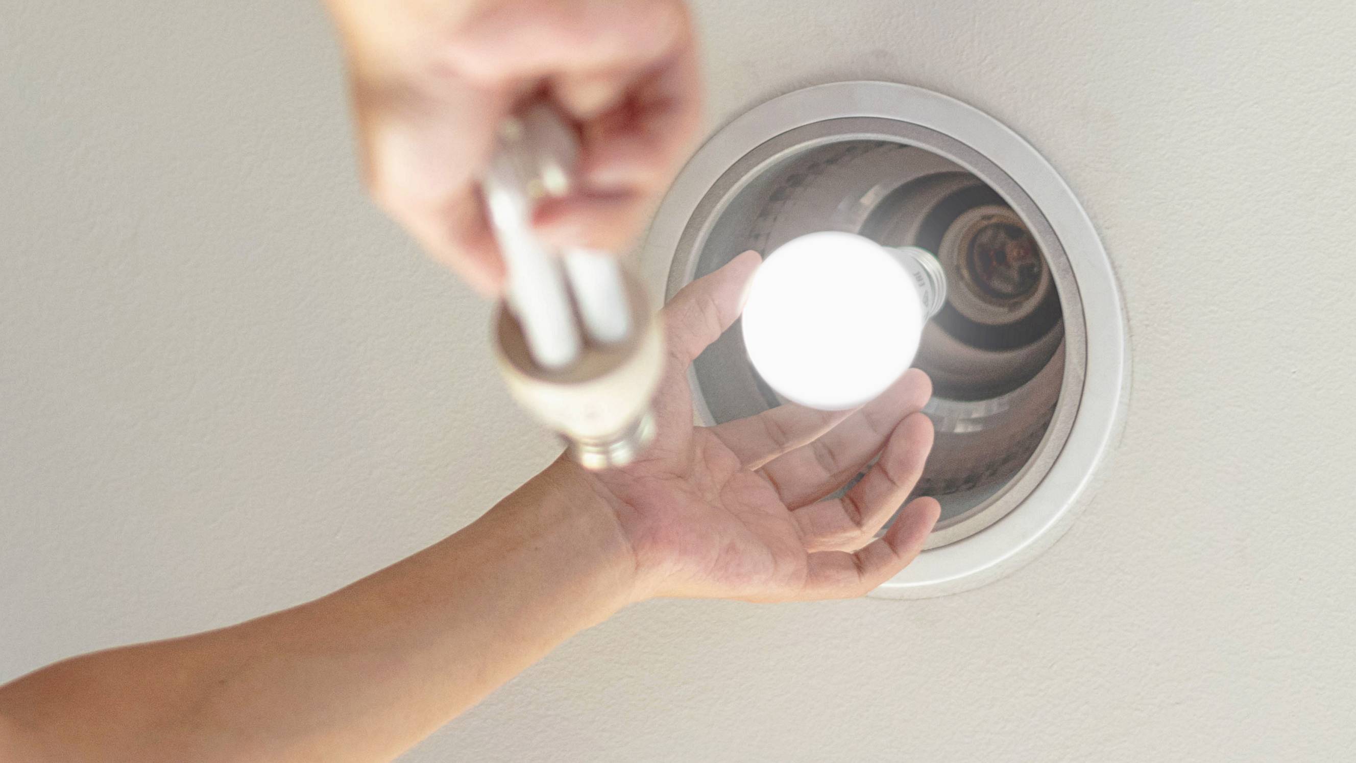 Man changing a fluorescent light bulb with an LED one