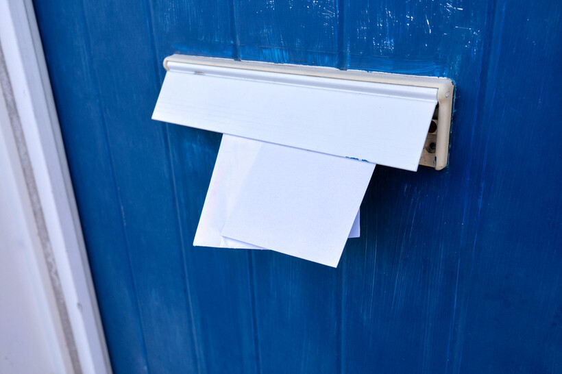 A close-up view of letters being held in a horizontal door-mounted letterbox. - how to replace a letterbox