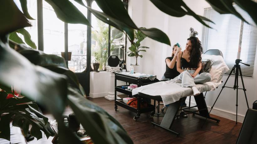 A female artist working on a client in a clean, well-lit studio. - how to make money as a tattoo artist