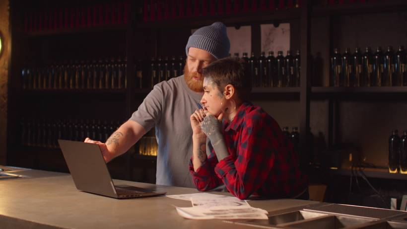 Tattoo owner and employee discussing admin tasks on a laptop. - make money as a tattoo artist