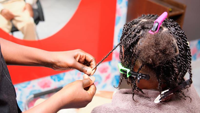 Stylist’s hands twisting a small section of hair while completing braids on a client with pink and green hair clips. - how much do dreadlocks cost