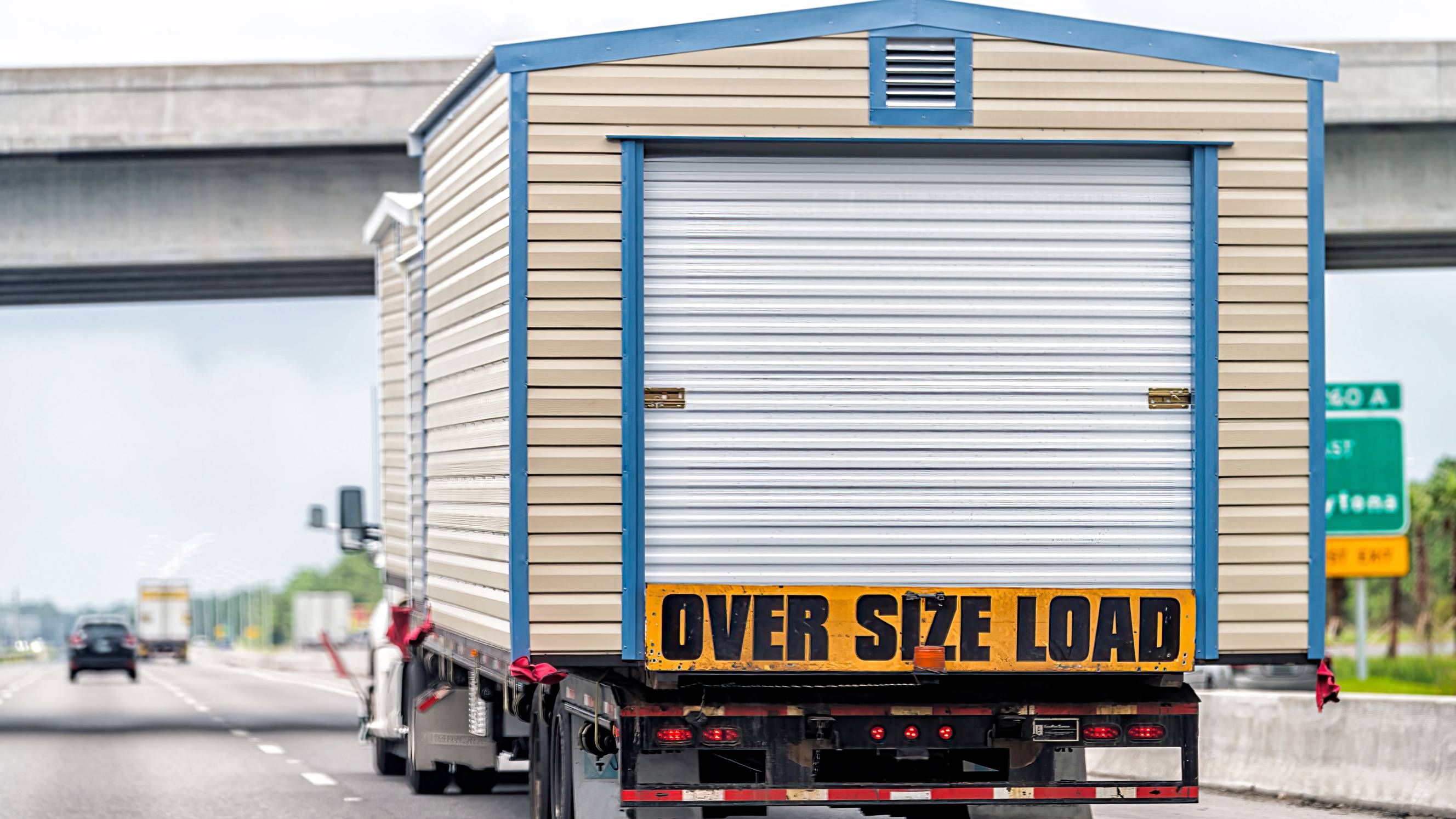 Rear view of a truck moving a prefabricated shed along the freeway