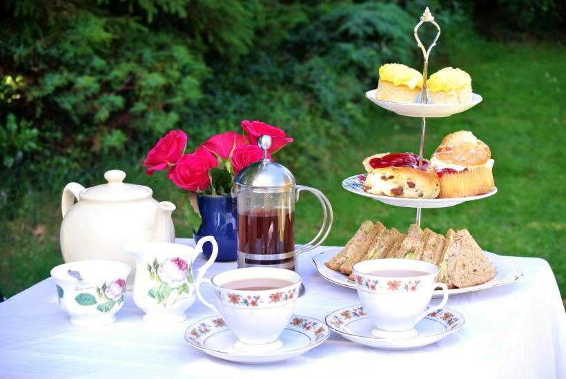 high tea vs afternoon tea - Traditional afternoon tea setup with tiered tray of cakes, scones, and sandwiches on a white tablecloth