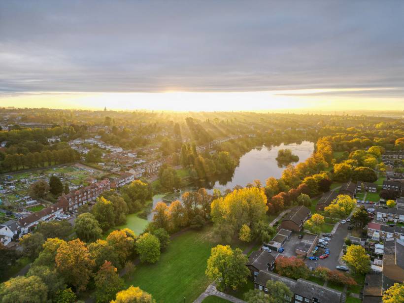 moving to Birmingham - Aerial view of Brookvale Park Lake surrounded by autumn trees and residential buildings at sunrise