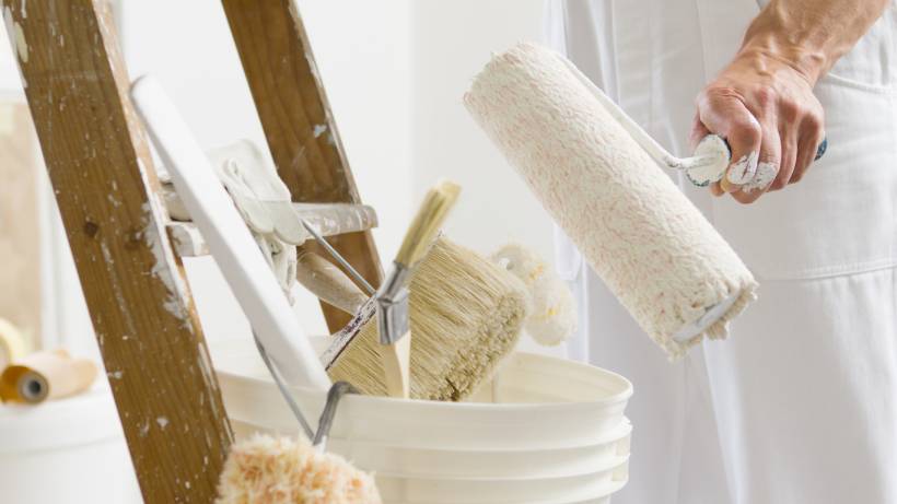 Painter holding a roller brush near a bucket with painting tools, representing Dulux Timeless vs Jasmine White paint choices