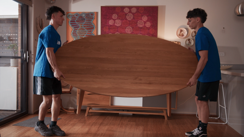 a pair of professional movers lifting a table and moving it into a new home. - moving checklist