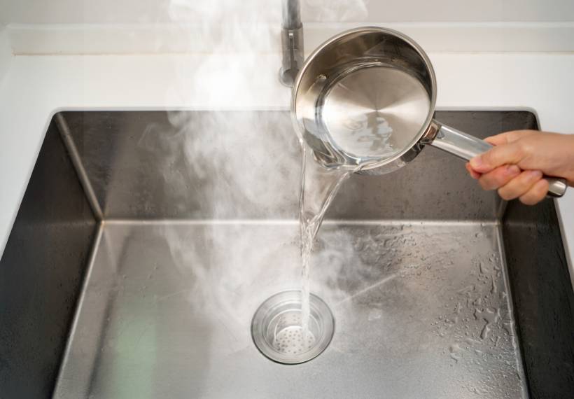 how to unclog drain - Pouring boiling water from a saucepan into a kitchen sink drain to help unclog it