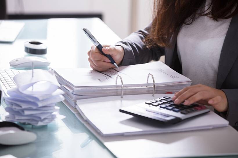 bookkeeper vs accountant - Bookkeeper reviewing financial documents and using a calculator at an office desk