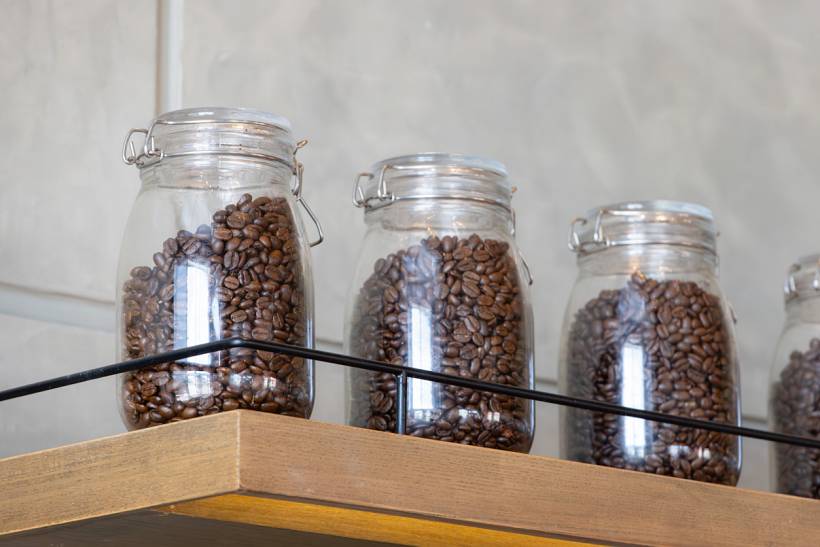 instant coffee vs. ground coffee - Glass jars filled with roasted coffee beans displayed on a wooden shelf