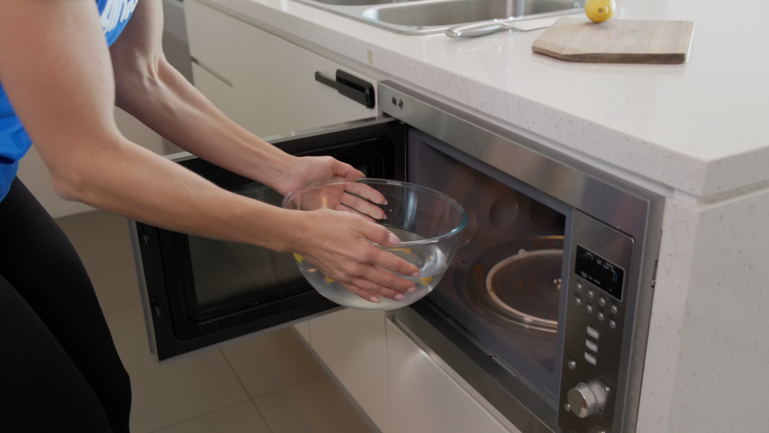 a Tasker putting a bowl of water with lemon inside a microwave to clean it