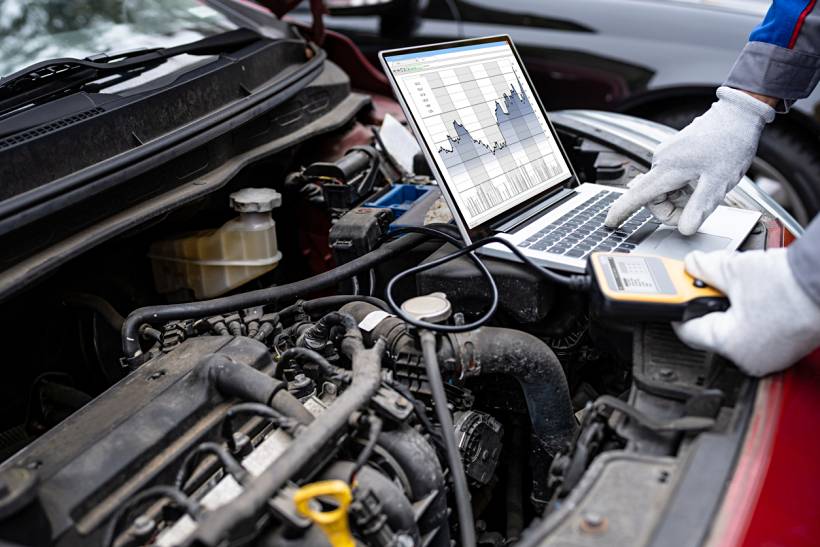 car diagnostic test cost - Technician using laptop and scan tool on car engine