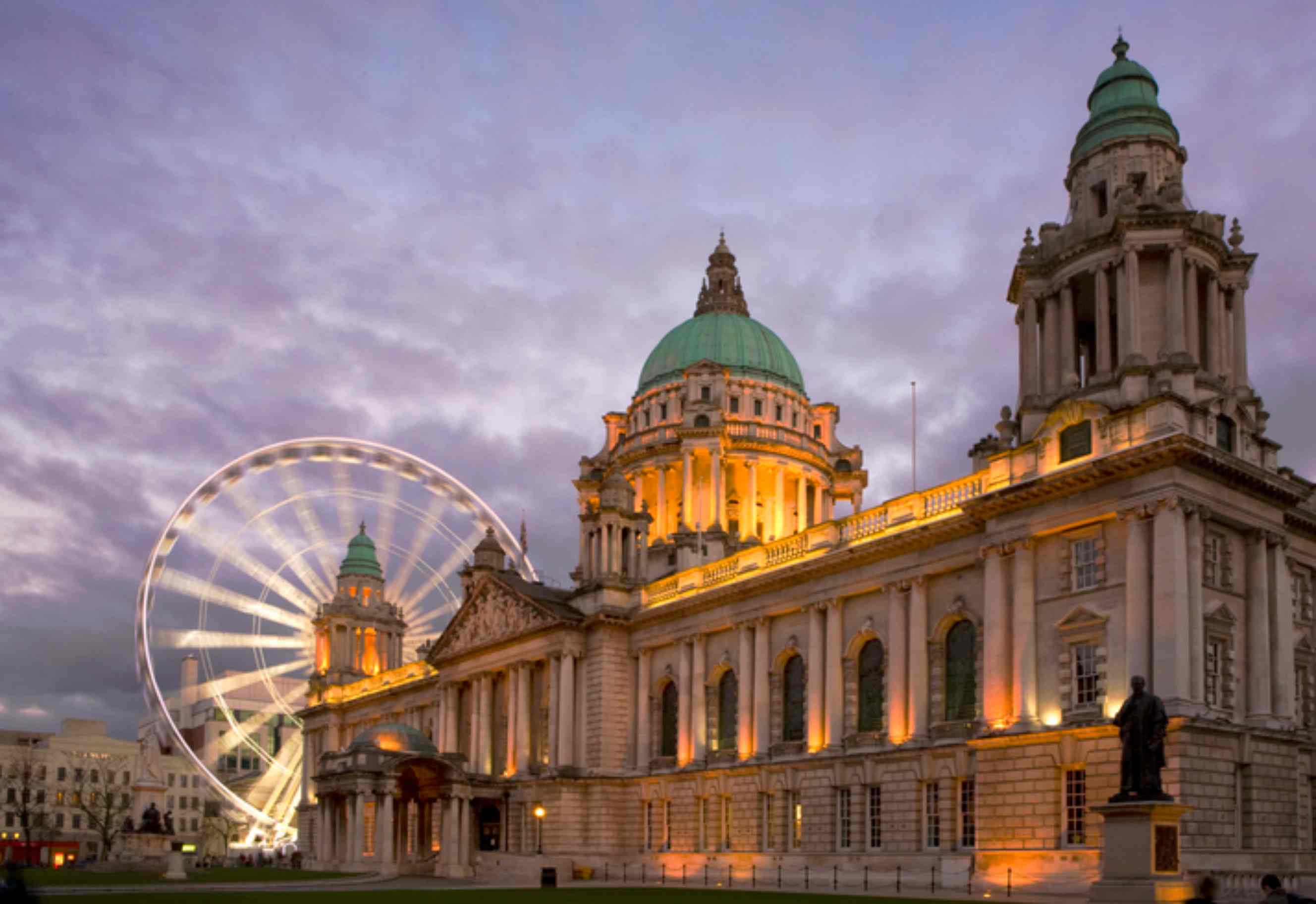 Belfast City Hall illuminated at dusk with the Belfast Wheel in the background