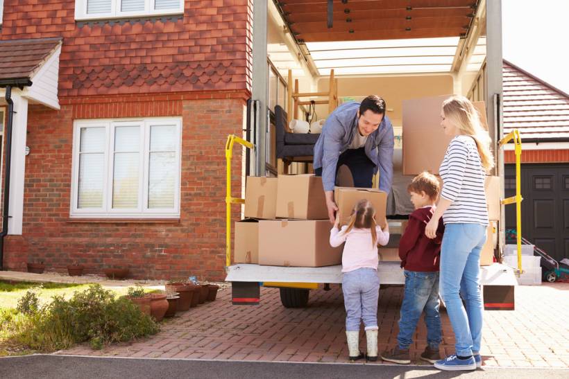 moving to Leeds - Parents and children carrying moving boxes beside a removal van at a suburban home
