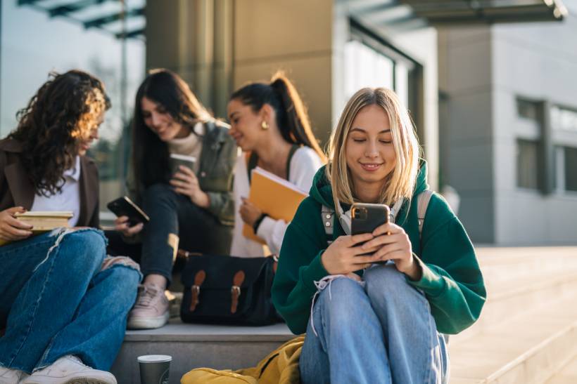 social media advertising cost - Student using a smartphone while sitting with friends outdoors