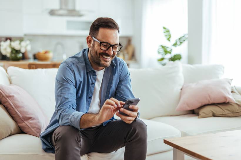 social media advertising cost - Smiling man browsing his phone in a bright living room