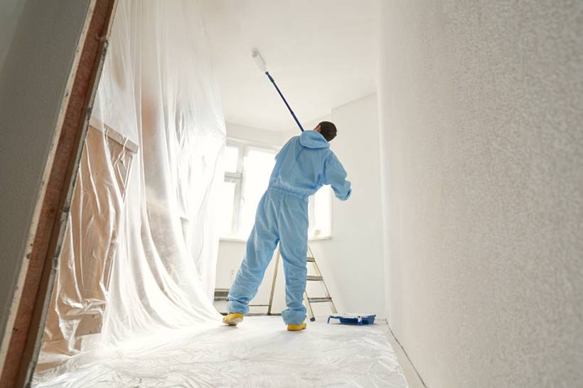 cost to paint interior of house - Painter using a roller on a ceiling in a protected room
