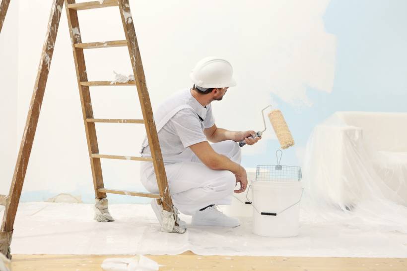 cost to paint interior of house - Painter applying white paint over a blue interior wall