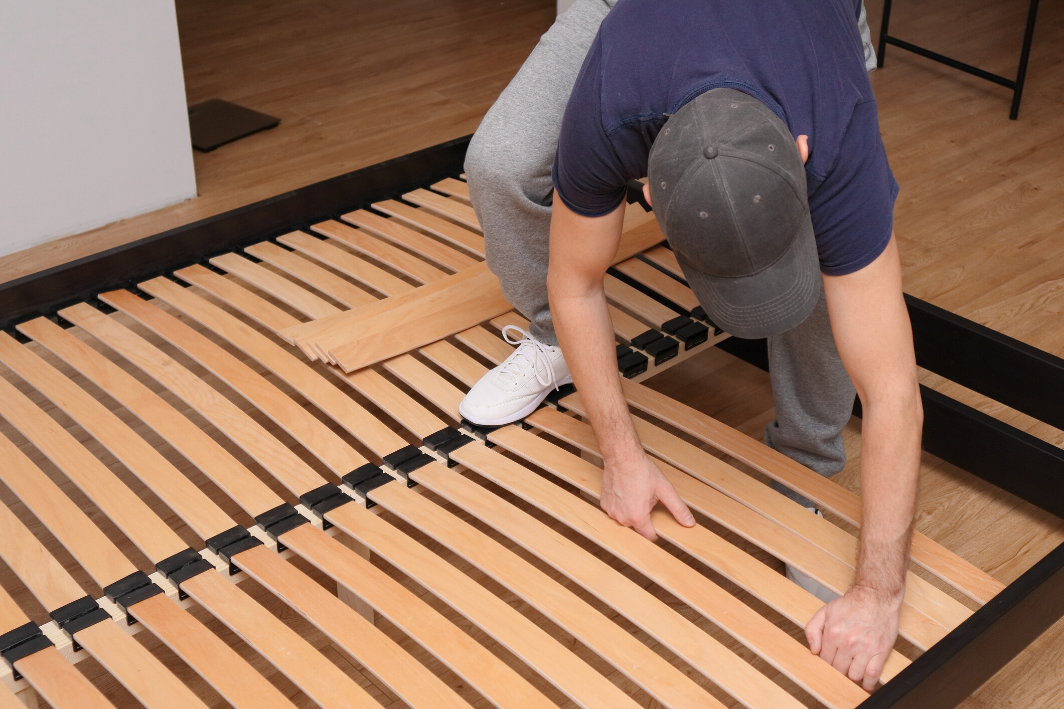 Man fitting wooden bed slats into a black bed frame during assembly