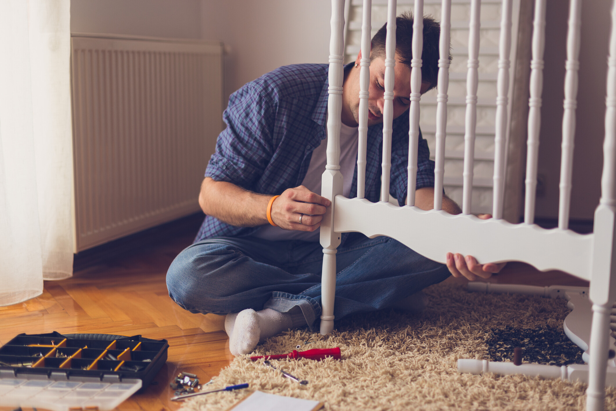 Man assembling a white wooden baby cot with spindle rails using hand tools