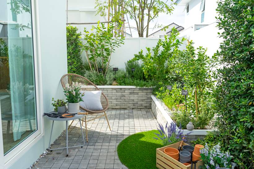 how much does a garden designer cost - Modern courtyard garden with paved patio, wicker chair, raised garden beds, and lush greenery
