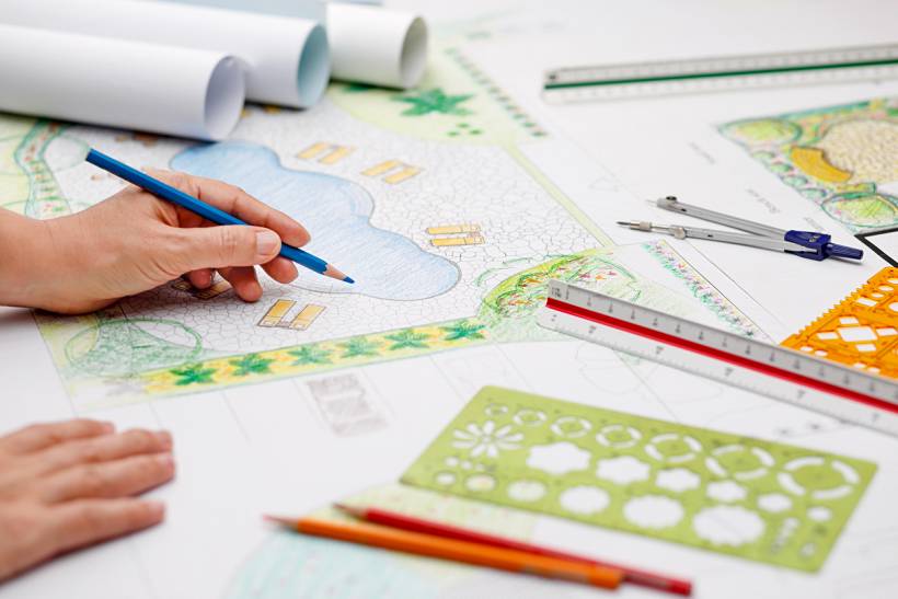 how much does a garden designer cost - Garden design in progress with hand-drawn landscape plans, coloured pencils, and drafting tools