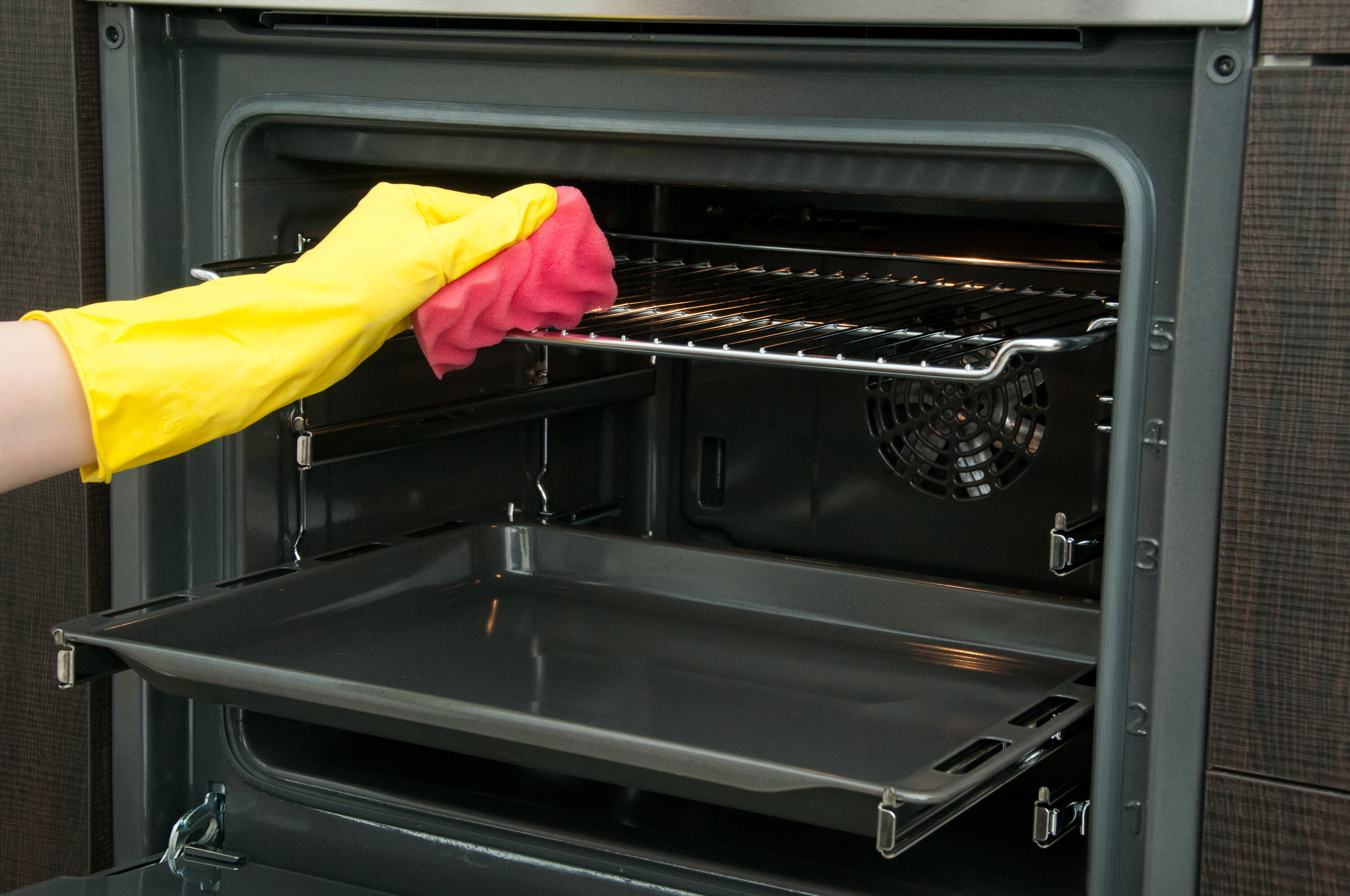 Close of a person cleaning an oven with yellow gloves