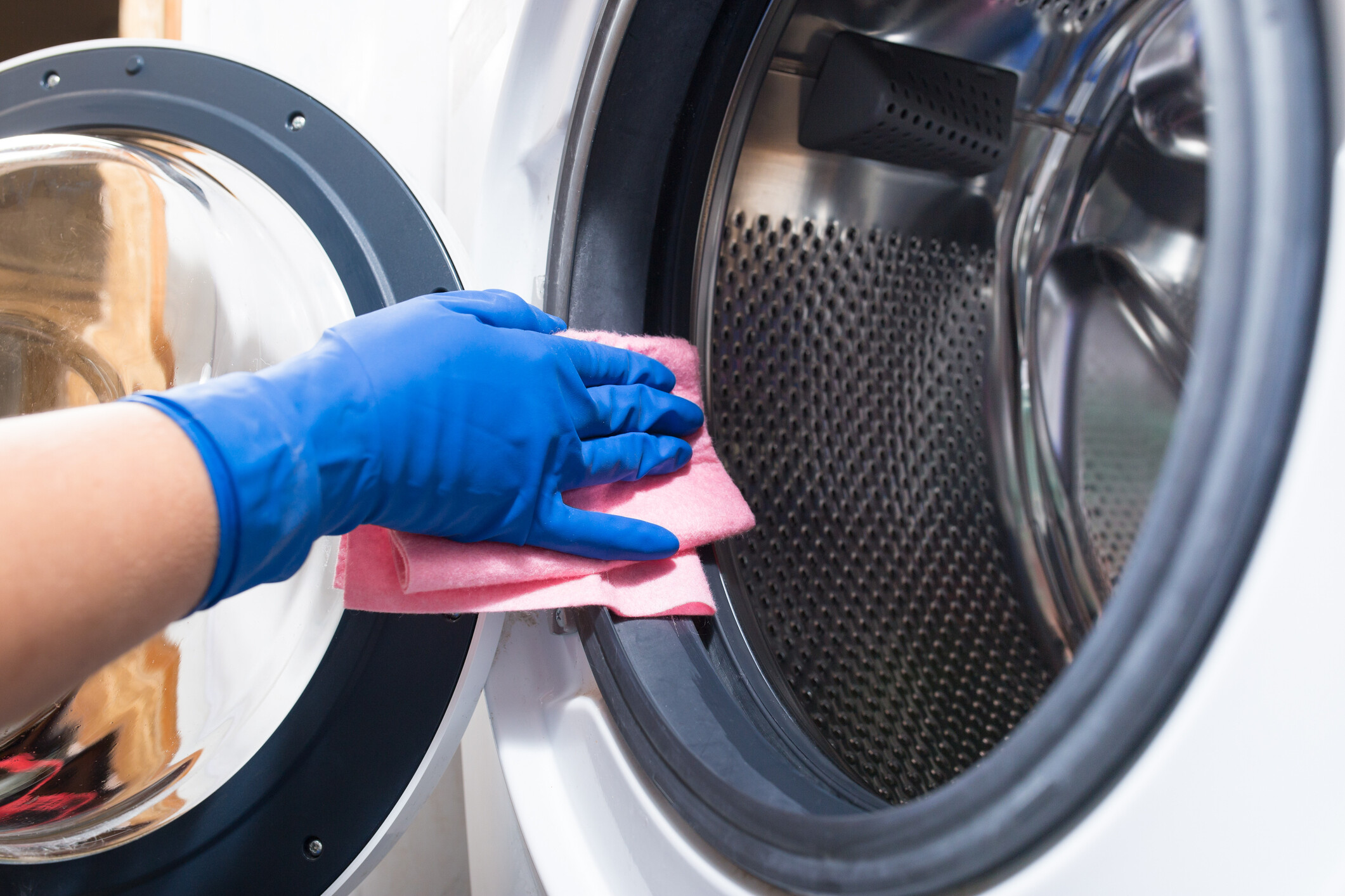 A person with blue gloves wiping the door of a washing machine.