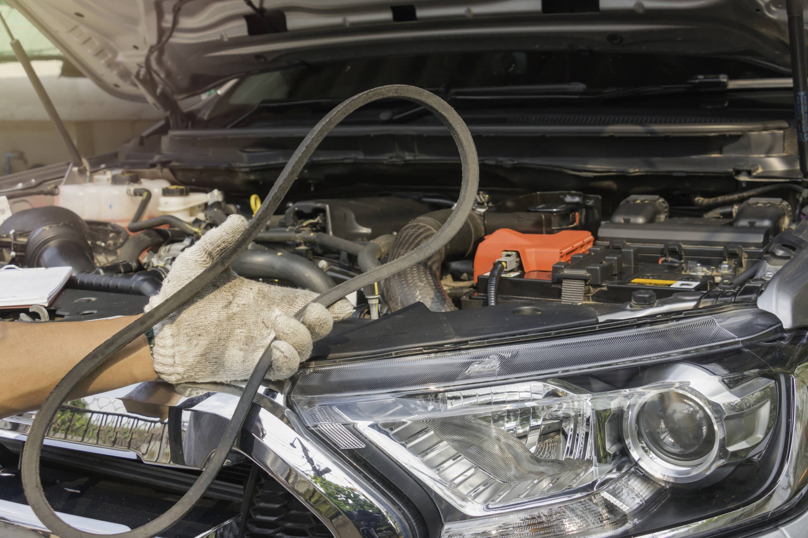 Mechanic holding a worn fan belt while preparing for a fan belt replacement in a car's engine bay.