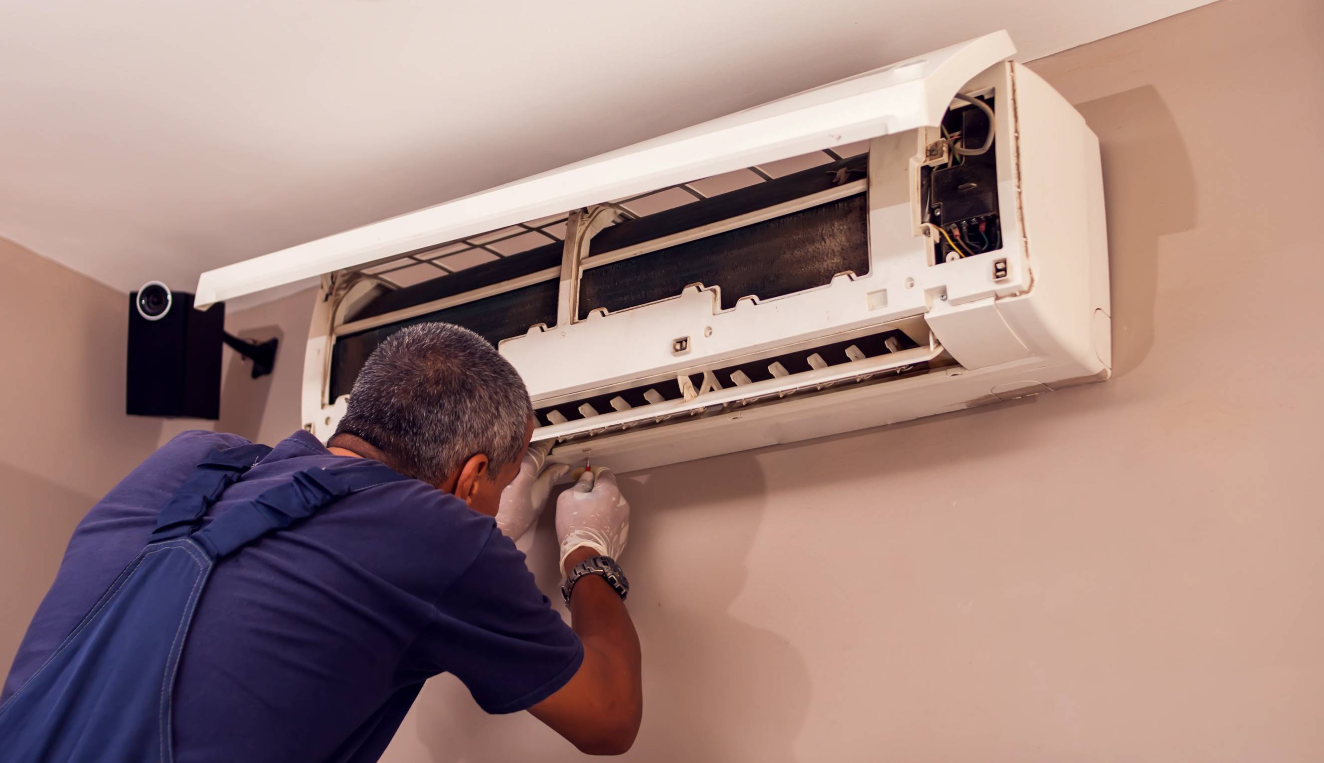 A handyman doing routine aircon servicing on a split-type AC unit.