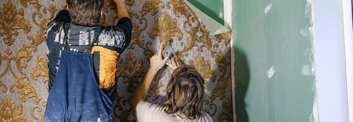 Two people carefully applying wallpaper to a wall, smoothing out the edges with a tool.