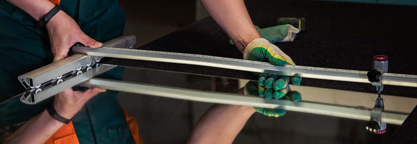 A person cutting a mirror with a glass cutter, creating precise lines on the reflective surface.