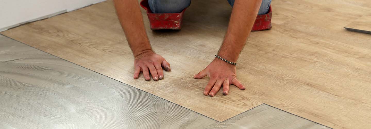 A close-up view of vinyl flooring with a wood grain pattern, being pressed down by a worker.