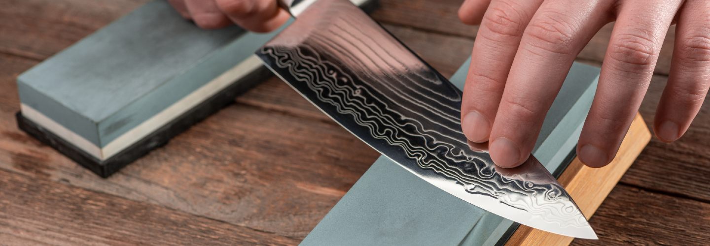 A close-up of a hand holding a knife against a sharpening stone.