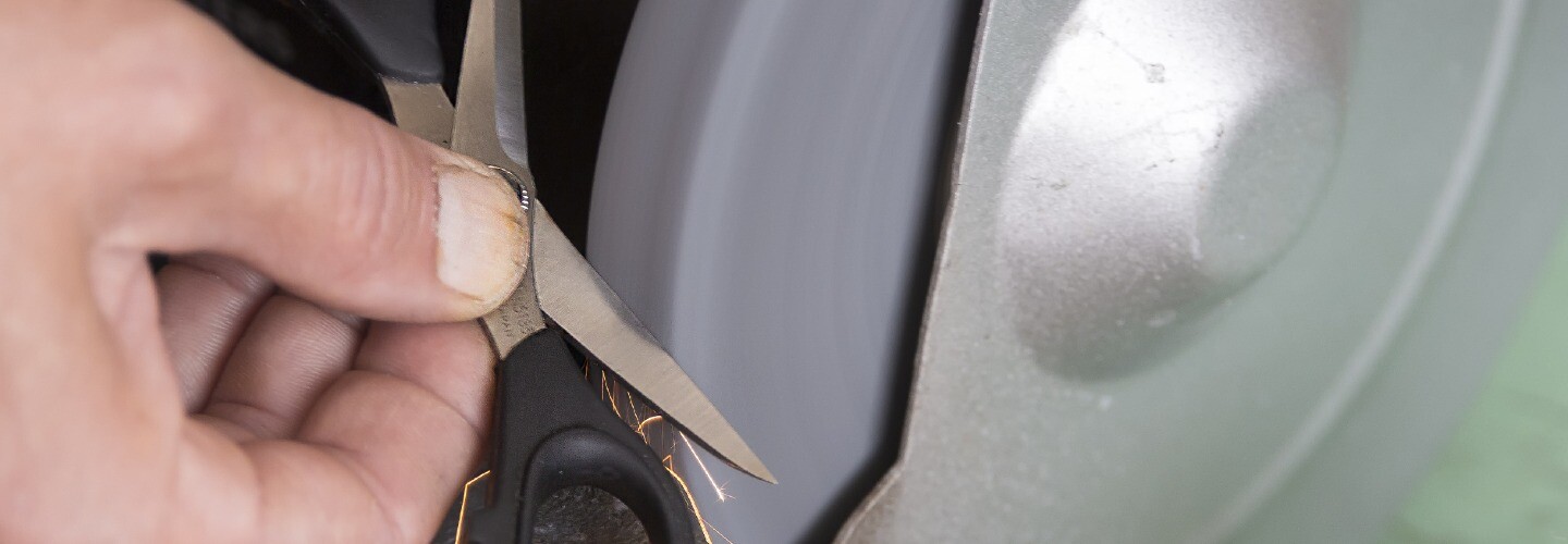 A close-up of a hand holding a pair of scissors, with sparks flying as they are being sharpened on a grinding wheel.