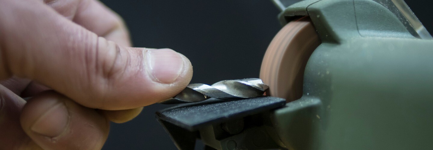 A close-up of a hand holding a drill bit tool against a sharpening tool.