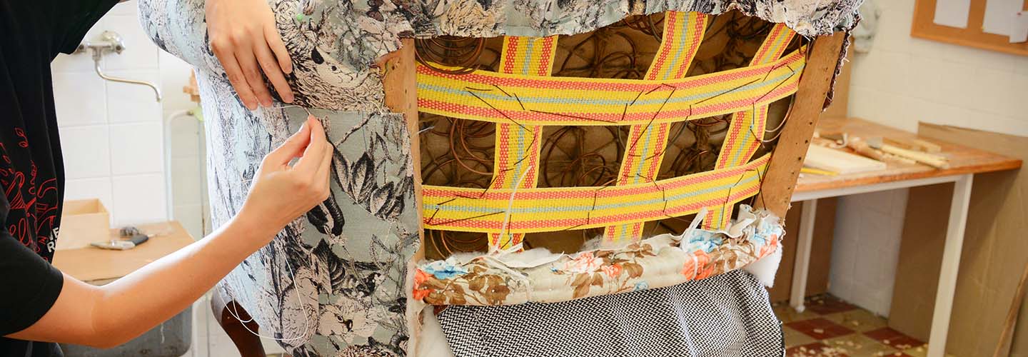 A professional upholsterer repairing a worn-out chair, using tools and fabric to restore its beauty and functionality.