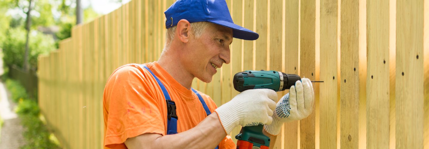 A close-up photo of a person installing a wooden fence.
