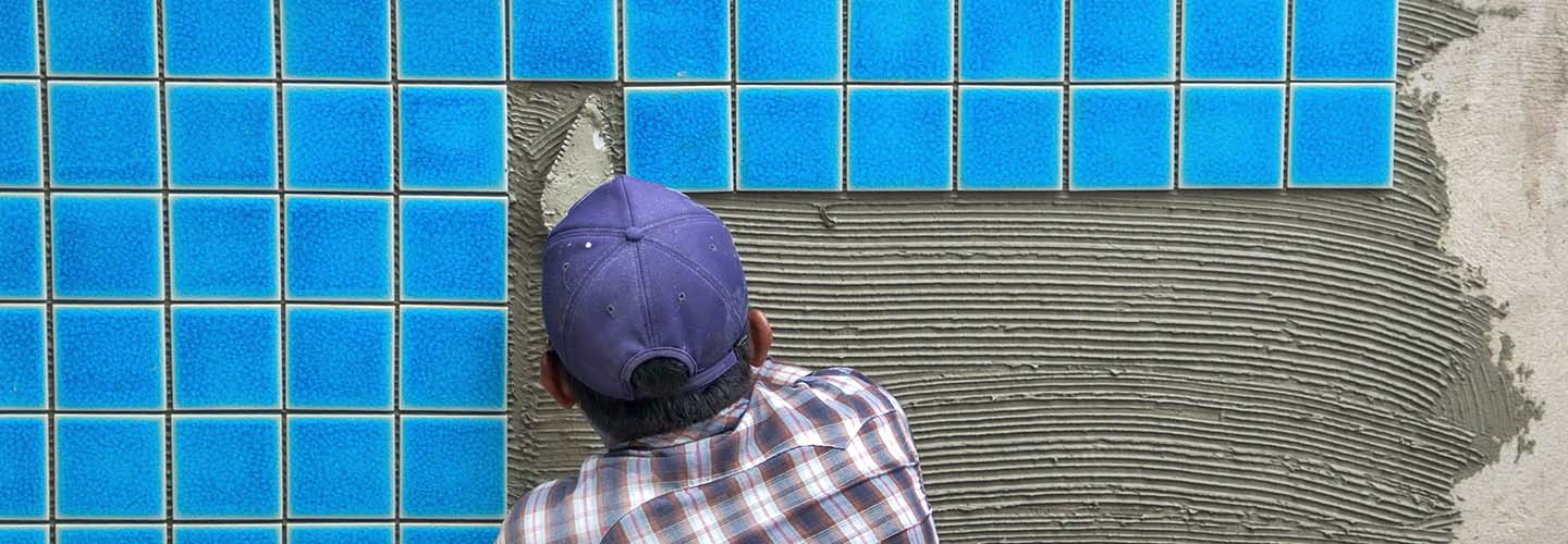 A person laying tiles on a swimming pool wall.
