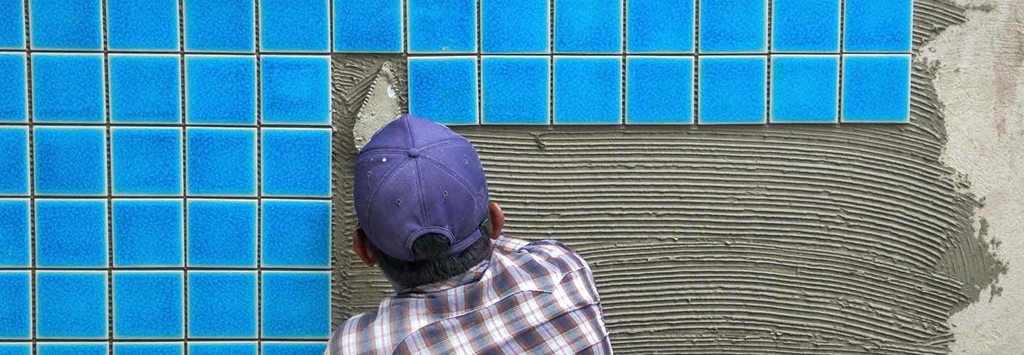 A person laying tiles on a swimming pool wall.
