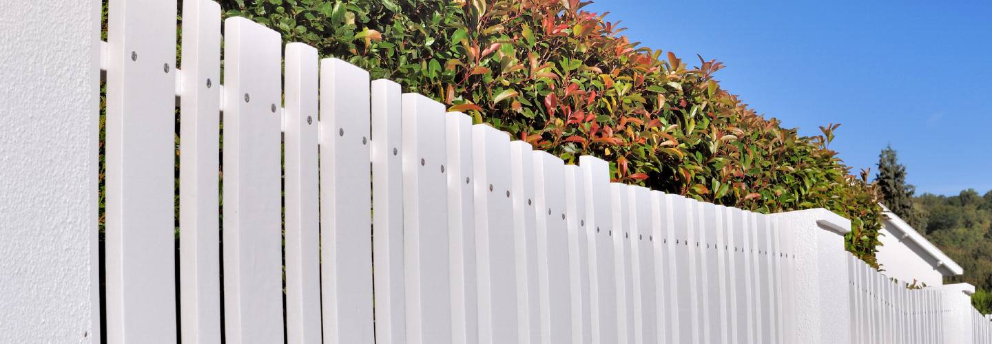 A white PVC fence surrounded by green bushes.