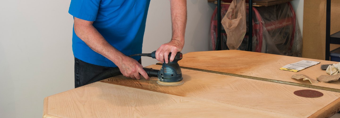 A person sanding a wooden table, preparing it for refinishing.