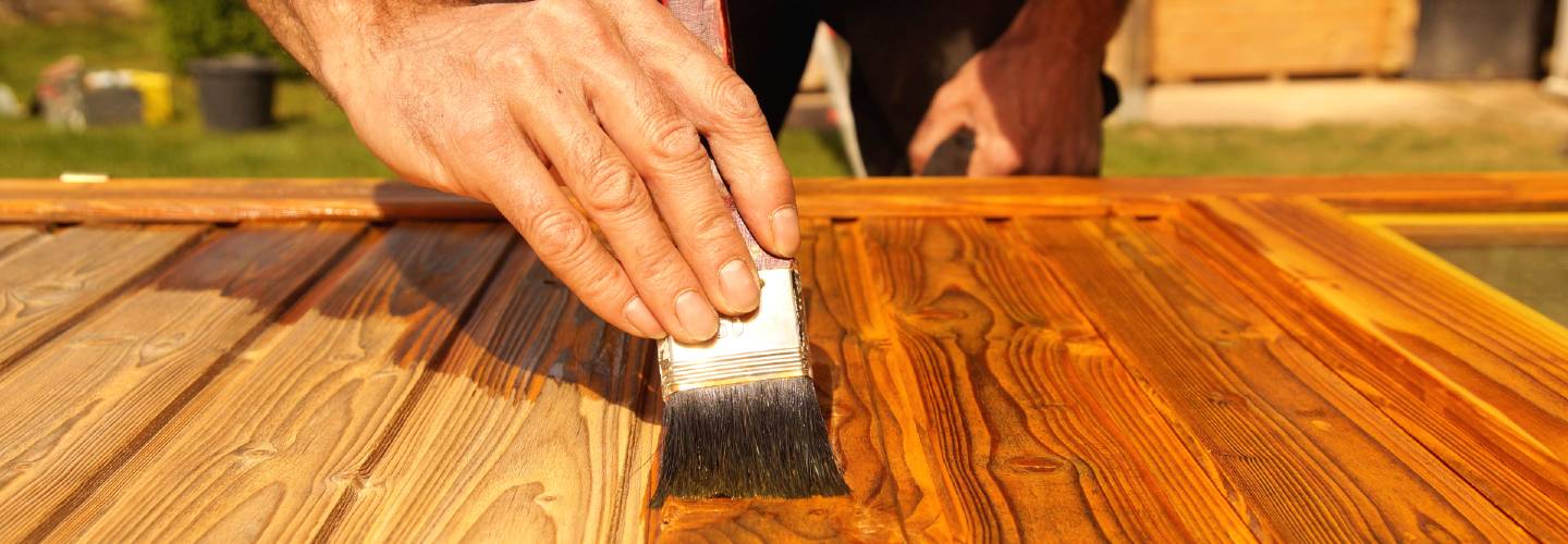 A person applying stain to a wooden surface with a brush, creating a smooth and even finish.