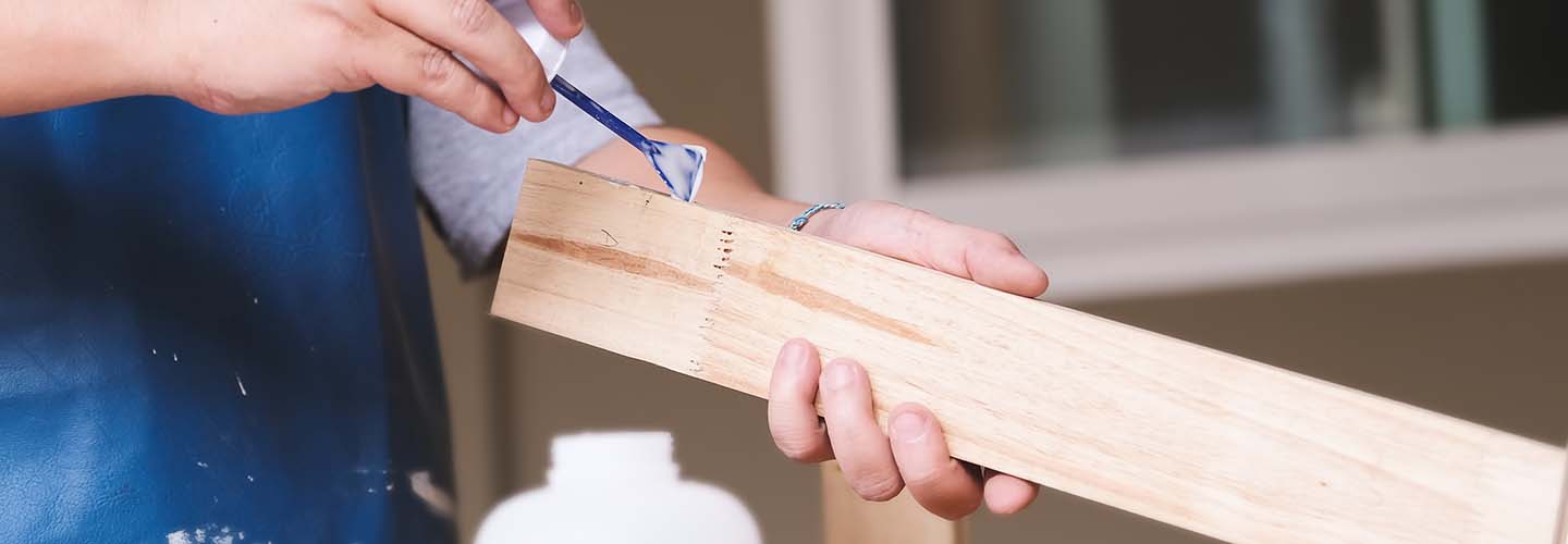 A close-up photo of a person's hand repairing a wooden surface with glue.